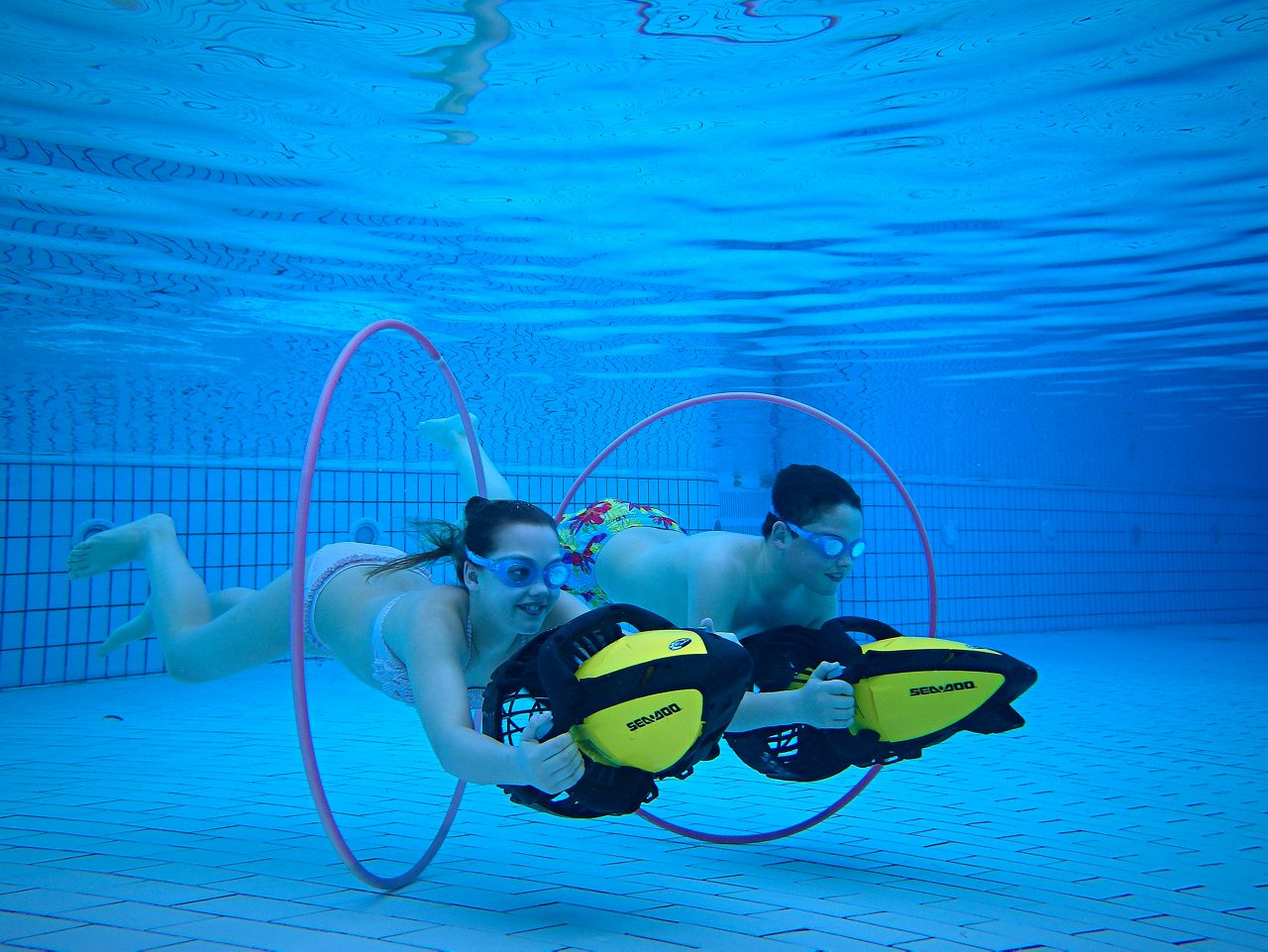 Two young people holding onto jets to swim through hoops in the pool.